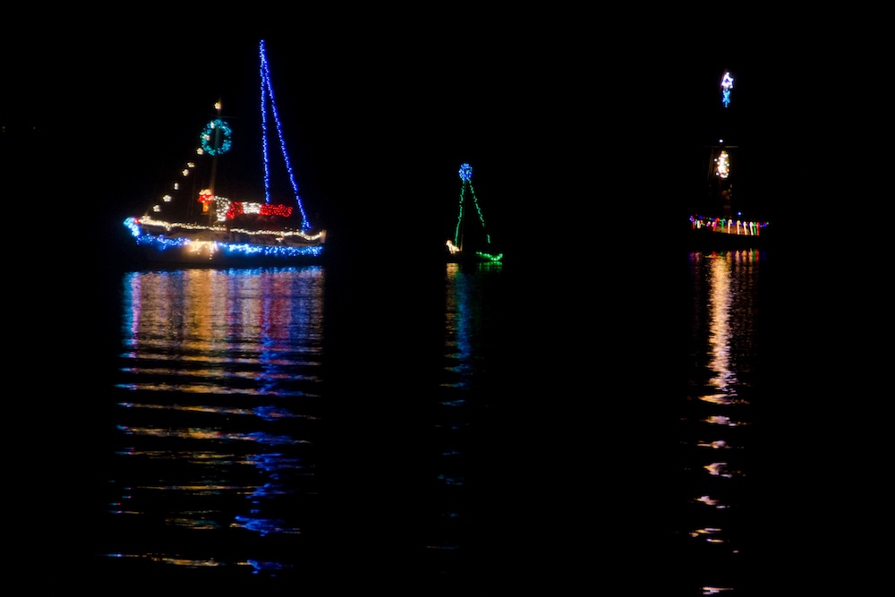 Sailboats covered in Christmas lights sailing across the water in the dark