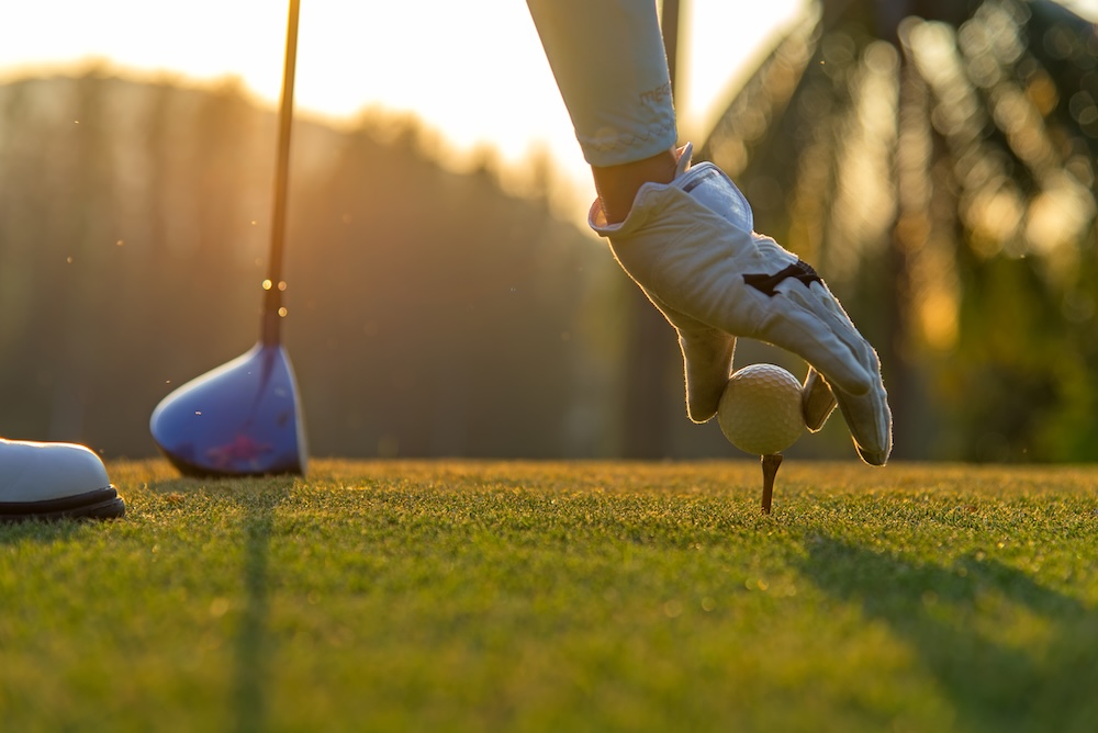 Closeup of a golfer's gloved hand placing a ball onto a tee